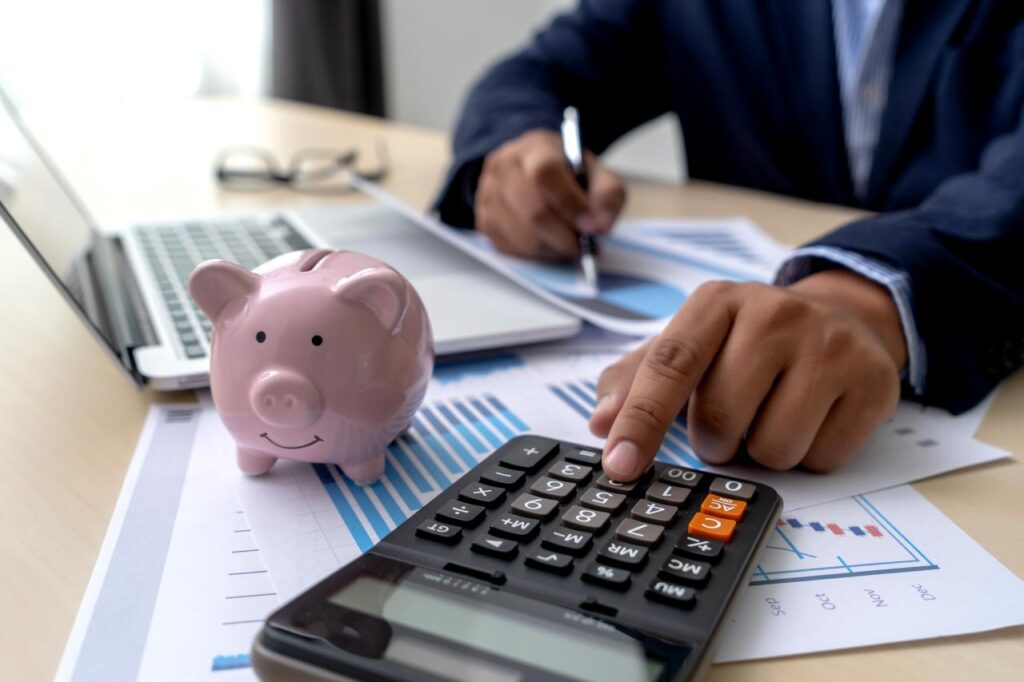 The hand of an accountant make a calculation using a calculator next to a piggy bank