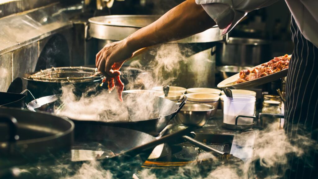 A chef de cuisine adds meat to a dish in a steaming pan.jpg