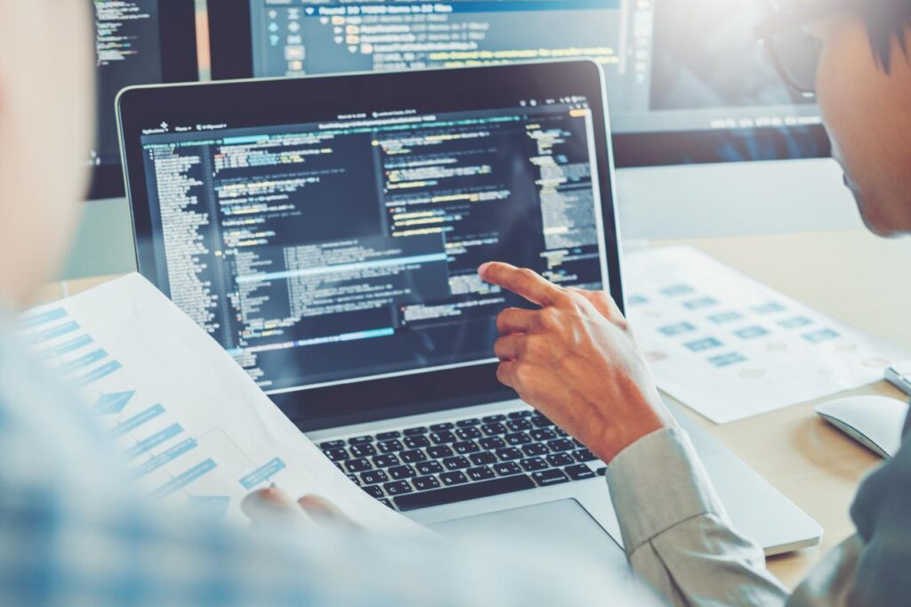 Software developers look at code on a laptop and compare written data