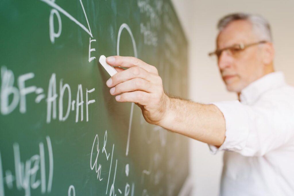 A male secondary school teacher demonstrates equations on a blackboard