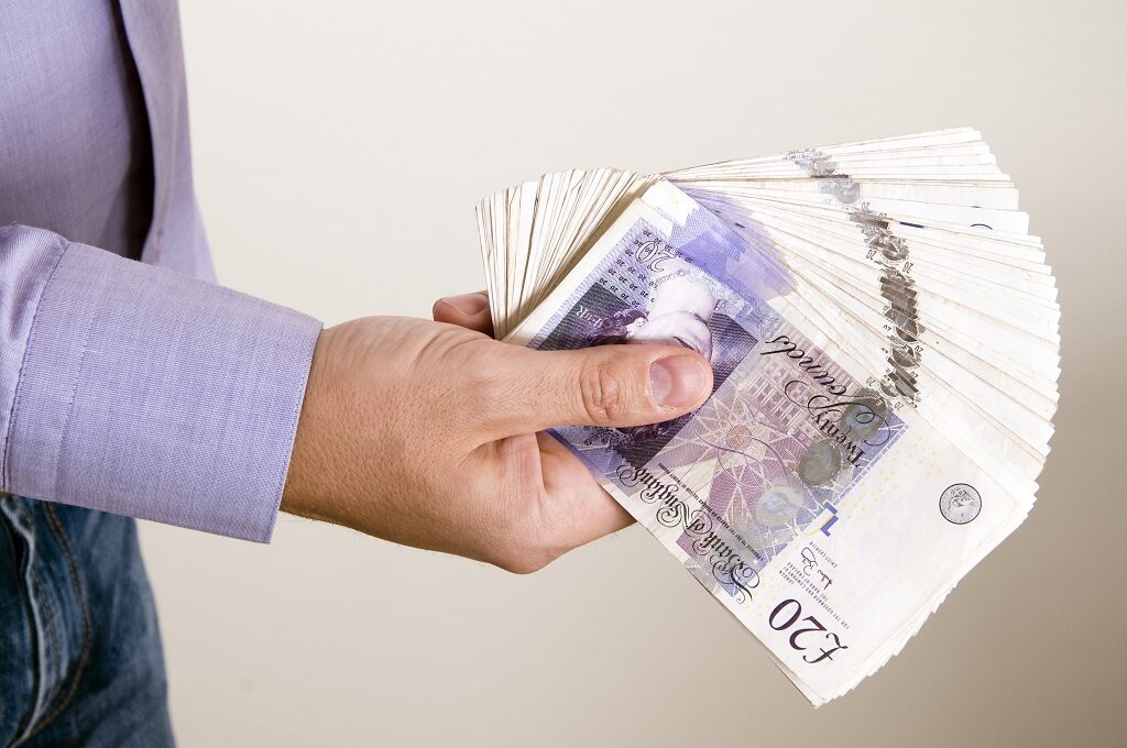 An employee holds a handful of £20 notes.