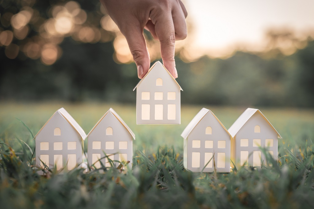 A hand choosing a paper representation of a house in a garden.